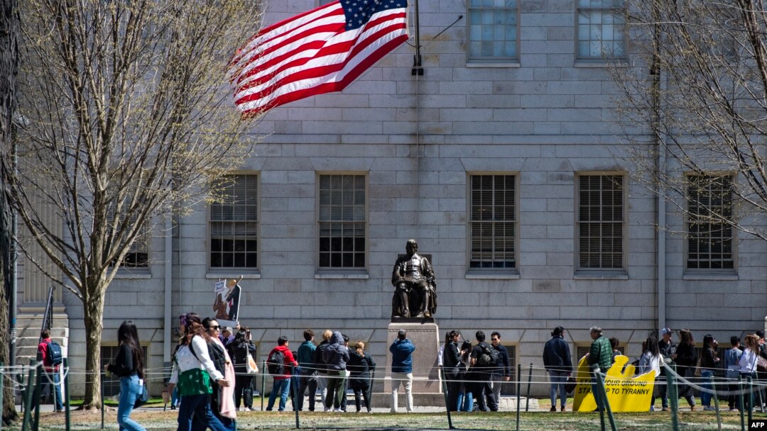 Protestatari cu placate adunați în fața statuii lui John Harvard în Harvard Yard, în urma unei demonstrații, pe 17 aprilie 2025.
