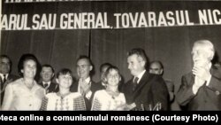 Nicolae Ceauşescu îi dă Nadiei Comăneci titlul de Erou al Muncii Socialiste şi medalia de aur Secera şi Ciocanul (19 august 1976). Sportiva fuge din țară la sfârșitul lunii noiembrie 1989. Sursa: Fototeca online a comunismului românesc. Cota: 168/1976