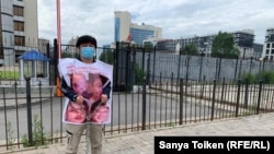 Акикат Калиолла стоит перед посольством Китая в Нур-Султане, заковав себя в цепи. Поверх его одежды — плакат с изображением родителей и братьев, оставшихся в Синьцзяне. 26 июня 2020 года