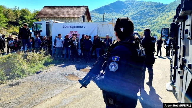 Disa zyrtarë të Policisë së Kosovës shihen afër disa protestuesve në Jarinjë, mbrapa të cilëve shihet mbishkrimi "Mirë se vini në Asociacionin e komunave serbe”.