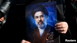 ქალს უჭირავს ირანის ახალი სასულიერო ლიდერის - მოჯთაბა ხამენეის პორტრეტი. 9 მარტი, 2026. თეირანი. აშშ-ისრაელის ირანის წინააღმდეგ ომის ფონზე მოჯთაბა ხამენეის დანიშვნის მხარდამჭერი შეკრება.