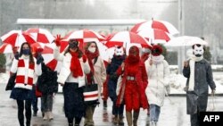 Жінки в карнавальних масках йдуть вулицями під парасольками кольорів біло-червоно-білого прапора Білорусі на знак протесту проти результатів виборів президента Білорусі в Мінську, 26 січня 2021 року