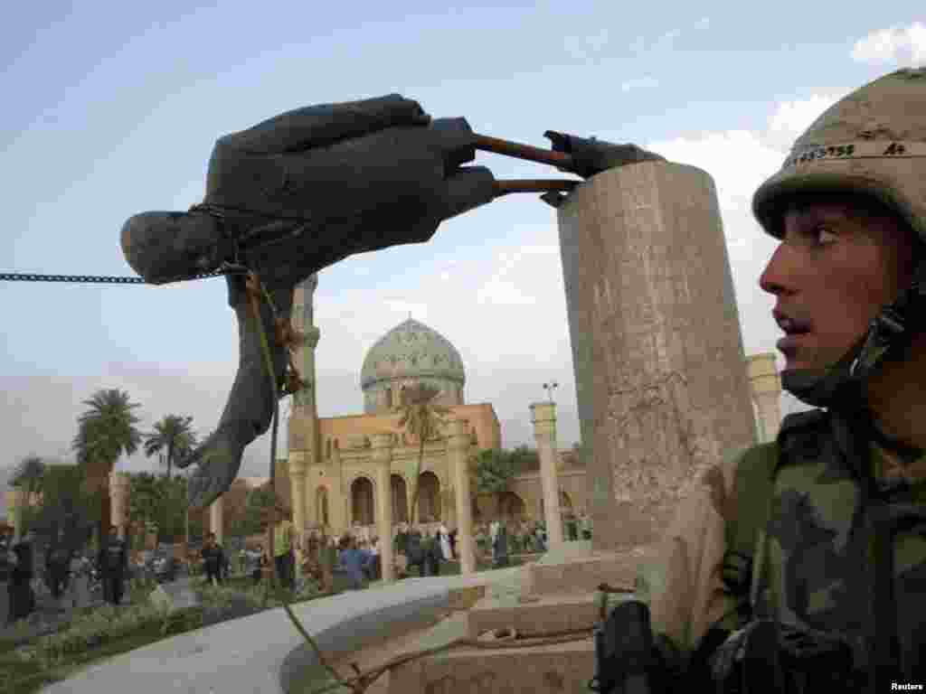 U.S. Marine Corp Assaultman Kirk Dalrymple watches as a statue of Iraq's President Saddam Hussein falls in central Baghdad April 9, 2003. U.S. troops pulled down a 20-foot (six meters) high statue of President Saddam Hussein in central Baghdad on Wednesday and Iraqis danced on it in contempt for the man who ruled them with an iron grip for 24 years. In scenes reminiscent of the fall of the Berlin Wall in 1989, Iraqis earlier took a sledgehammer to the marble plinth under the statue of Saddam. Youths had placed a noose around the statue's neck and attached the rope to a U.S. armoured recovery vehicle. REUTERS/Goran Tomasevic 