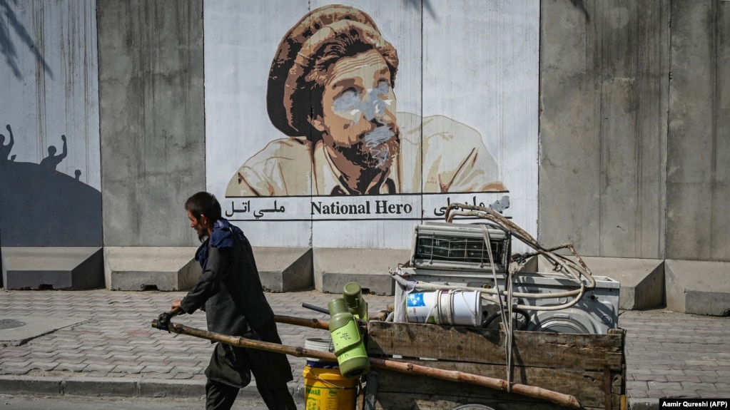 A man pushes his cart past a portrait of late Afghan commander Ahmad Shah Masud that was defaced with spray paint in Kabul.