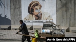 A man pushes his cart past a portrait of late Afghan commander Ahmad Shah Masud that was defaced with spray paint in Kabul.