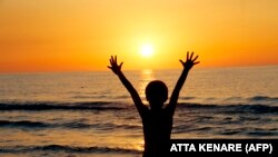 Iran -- An Iranian child raises his hands at sunset at a beach in the Caspian Sea port city of Mahmoud Abad, in northen Mazandaran province on June 16, 2016. / AFP PHOTO / ATTA KENARE