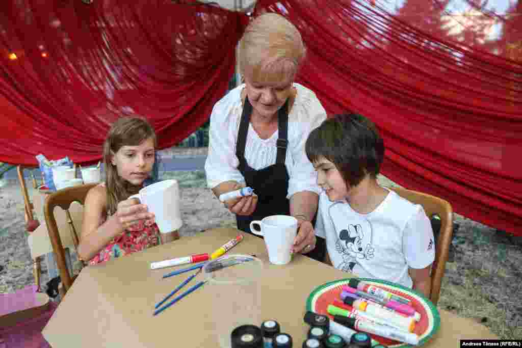 Artistul vizual Daniela Frumușeanu (C) le învață pe Iustina (S) și Nur (D) să picteze pe căni din ceramică înaintea concertului de deschidere a festivalului &bdquo;Promenada Operei&rdquo;.