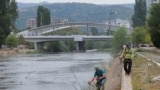 Punëtorë duke kositur bar buzë lumit Ibër, afër urës kryesore të qytetit të ndarë etnikisht, në Mitrovicë, më 9 shtator 2024.