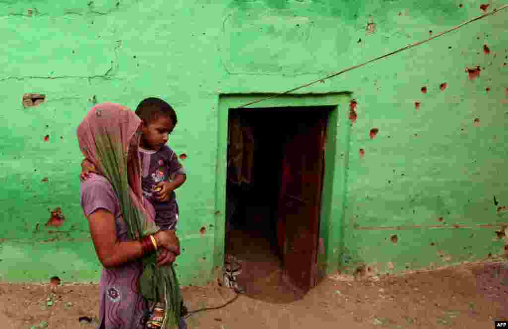 An Indian villager carries a child past a pock-marked house where four members of a family were reported to have been killed in cross-border exchanges, in Mashe de Kothe village, some 55 kilometers from Jammu.
