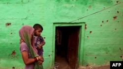 An Indian villager carries a child past a house where four members of a family were reported to have been killed in cross-border firing between Indian and Pakistani soldiers at Mashe de Kothe village in Arnia sector near the India-Pakistan border.