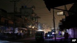 People and auto rickshaws are silhouetted on vehicles' headlights on a dark street during widespread power outages in Rawalpindi on January 10.