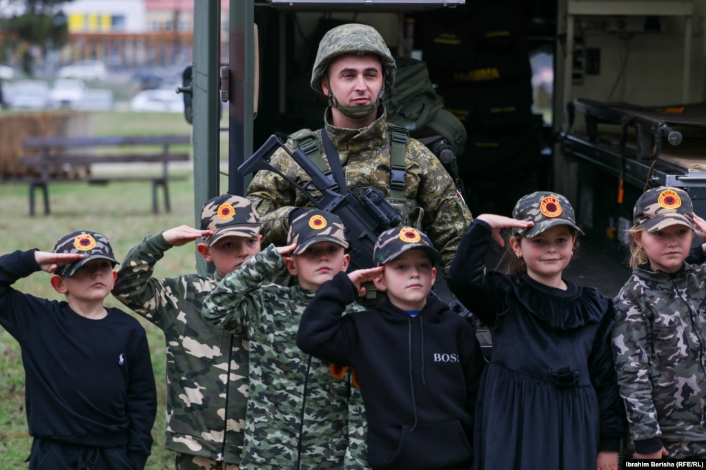 Fëmijë të veshur me rroba të stilit ushtarak dhe me kapele me emblëm e UÇK-së fotografohen së bashku me një ushtar të FSK-së. 