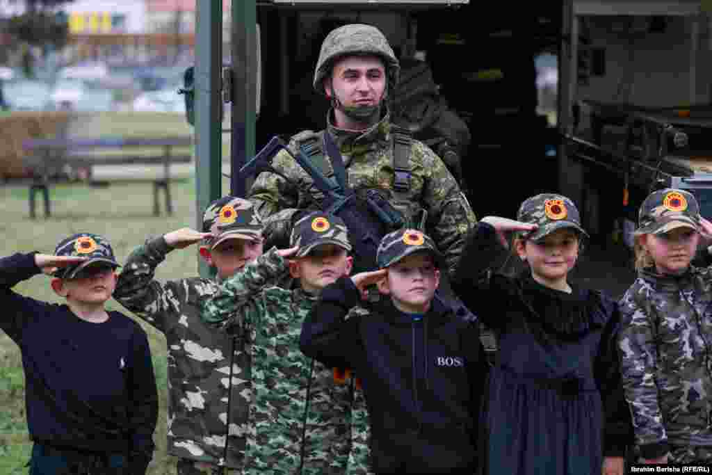 Fëmijë të veshur me rroba të stilit ushtarak dhe me kapele me emblëm e UÇK-së fotografohen së bashku me një ushtar të FSK-së. 