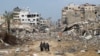 گروهی از مردم نوار غزه در حال عبور از مقابل ساختمان‌های ویران‌شده بر اثر بمباران‌های اسرائیل/ ۱۳ دی
