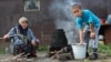 Жена и сын Зулкайнара Ергашева кипятят воду для чая на огне на улице, экономя газ. Семья переехала с юга на север Казахстана два месяца назад. Село Покровка, 21 июля 2016 года.