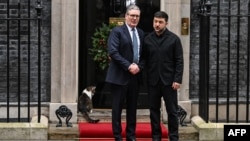 Прем'єр-міністр Великої Британії Кір Стармер (л) вітає президента України Володимира Зеленського на порозі своєї резиденції у час, коли кіт Ларрі чекає, щоб його впустили до будинку на Даунінґ-Стріт, 10, грудень 2025 року