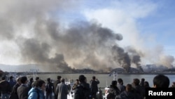 Onlookers watch as smoke rises from South Korea's Yeonpyeong Island after it was hit by dozens of artillery shells fired by North Korea on November 23.