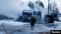 Vatrogasac ispred kamiona uništenih tokom ruskih napada dronovima i raketama na Kijev, 24. januar 2026.