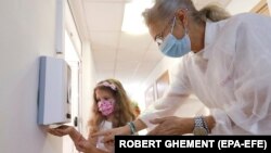 Zdravstvena radnica pokazuje djevojčici kako da koristi sredstvo za dezinfekciju ruku tokom prvog dana škole na Nacionalnom muzičkom koledžu 'George Enescu' u Bukureštu, Rumunija (14. septembar 2020.)