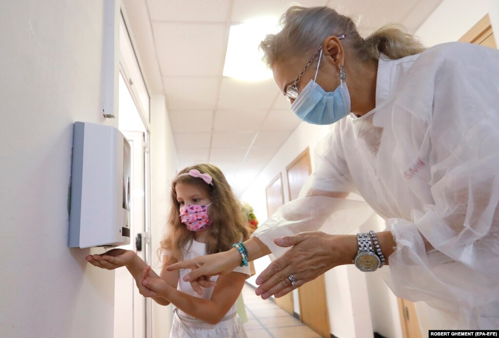 Медичний працівник показує дівчинці, як потрібно користуватися засобом для дезінфекції рук