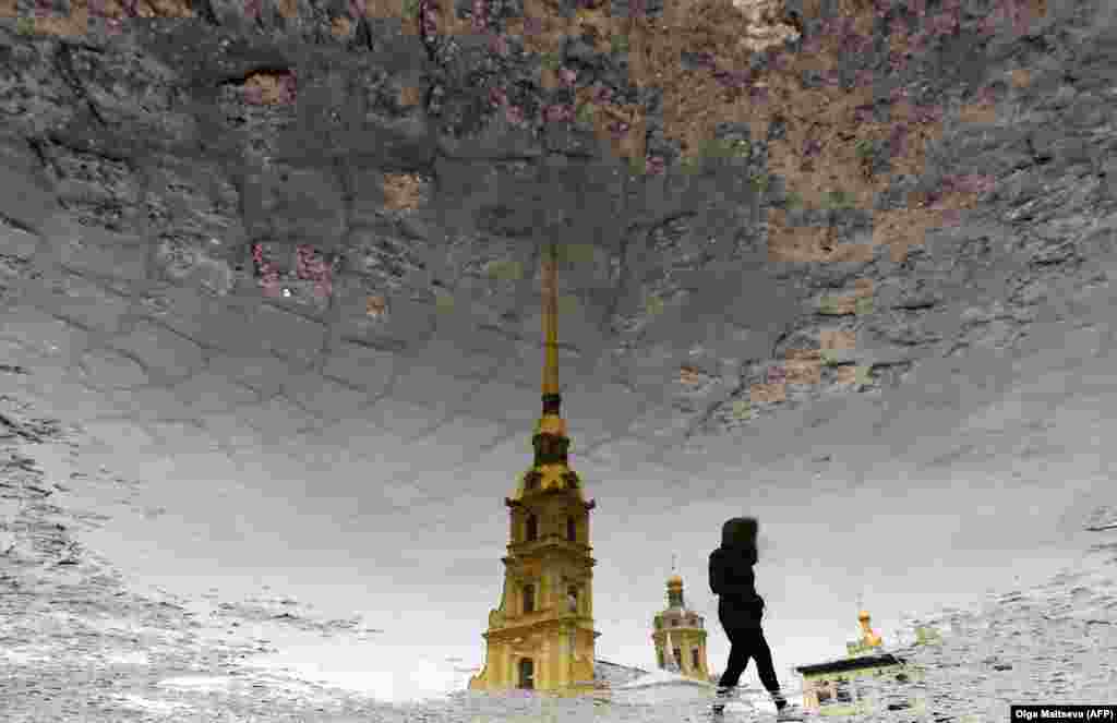 The silhouette of a woman is reflected in a puddle as she crosses a square in front of Saints Peter and Paul Cathedral in St. Petersburg, Russia. (AFP/Olga Maltseva)