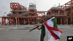 March 16, 2019 photo, an Iranian worker carries Iranian flags prior to an inauguration ceremony of a natural gas refinery at the South Pars gas field on the northern coast of the Persian Gulf, in Asaluyeh, Iran.