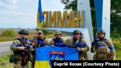 Ukrán katonák a felszabadított Limant jelző táblánál 2022. október 2-án