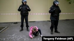 A young girl writes "I'm for the park" on the asphalt in front of a fence designed to block demonstrators protesting plans to construct a cathedral in a park in Yekaterinburg on May 16.