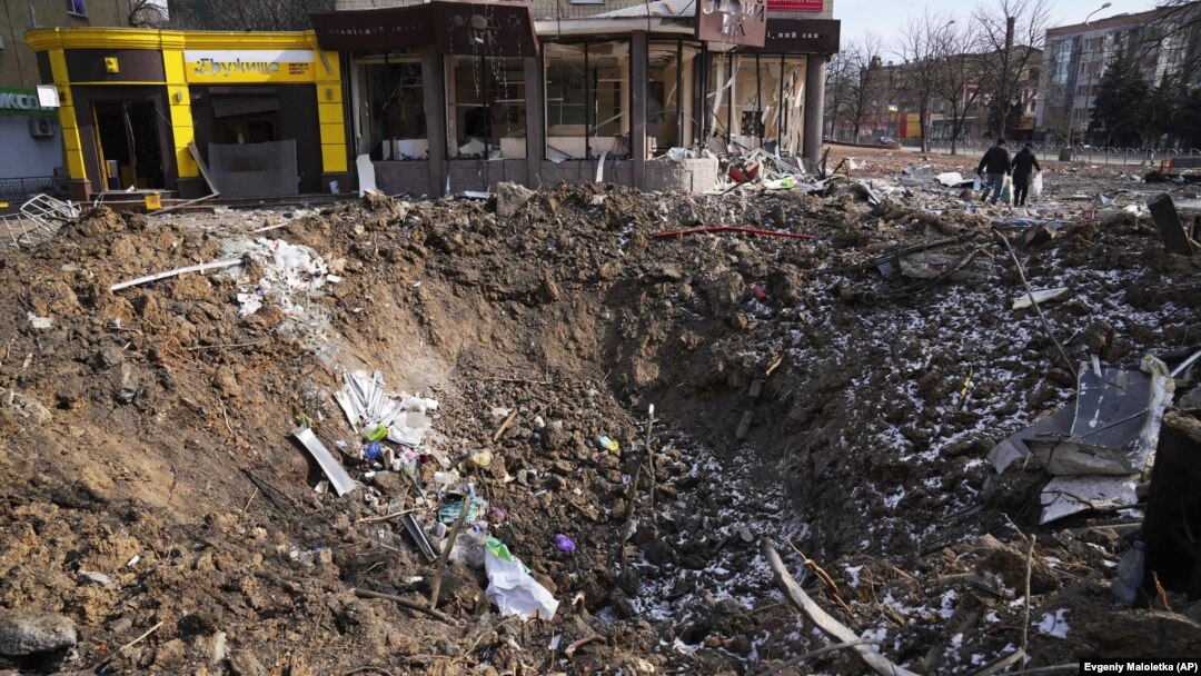 People walk past a shell crater on Mariupol's Avenue Of Peace on March 13. 