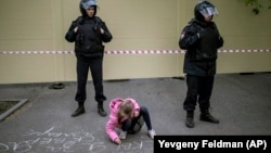 A young girl writes "I'm for the park" on the asphalt in front of a fence designed to block demonstrators protesting plans to construct a cathedral in a park in Yekaterinburg on May 16.