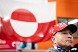 Ларс Йорген Клейст, один из лидеров политической партии "Сиумут", выступающей за тесное сближение с США, в кепке MAGA на фоне флага Гренландии во время парламентских выборов. 11 марта 2025 года