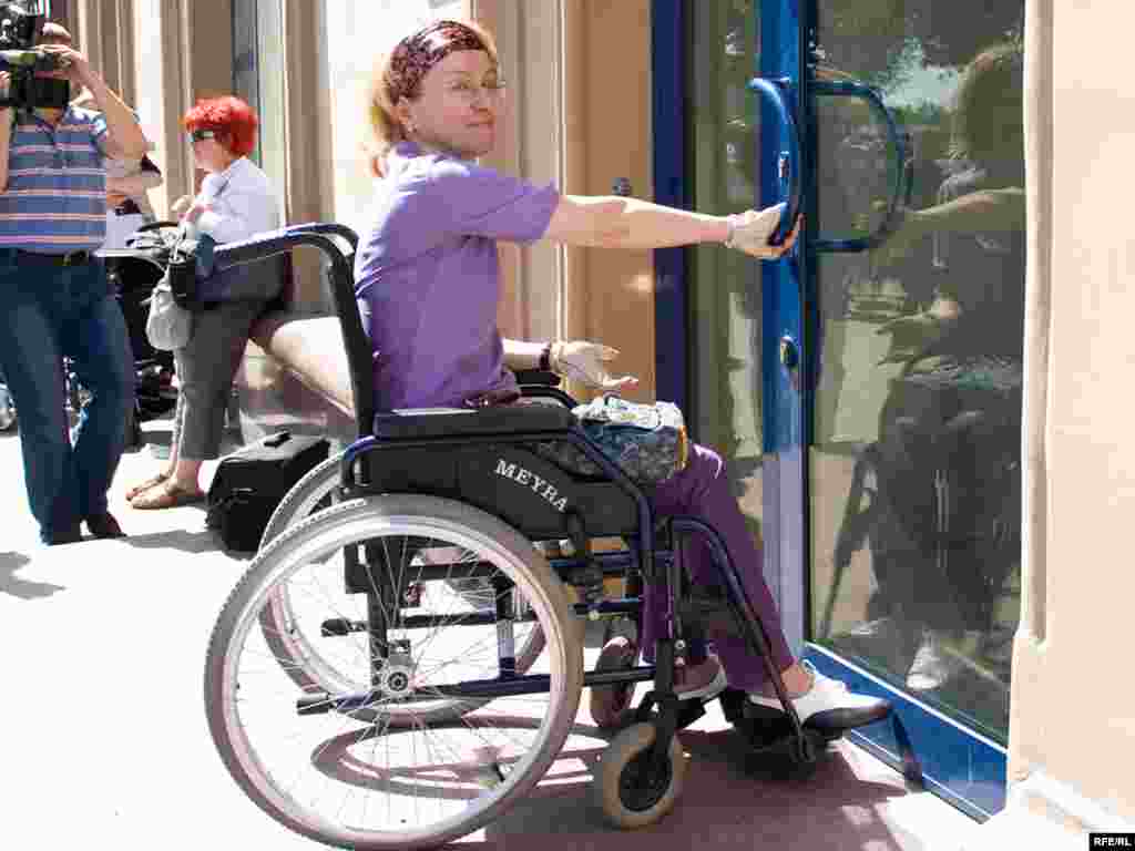 Одна из организаторов акции экономист Ирина Ясина показывает, что инвалидам-колясочникам невозможно без посторонней помощи открыть дверь в магазин...