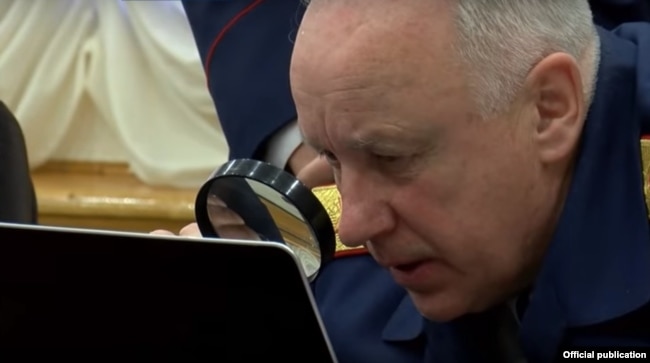Глава Следственного комитета Александр Бастрыкин с лупой у экрана компьютера.