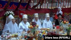 Наурыз мейрамына жайылған дастархан басында отырған адамдар. (Көрнекі сурет.)