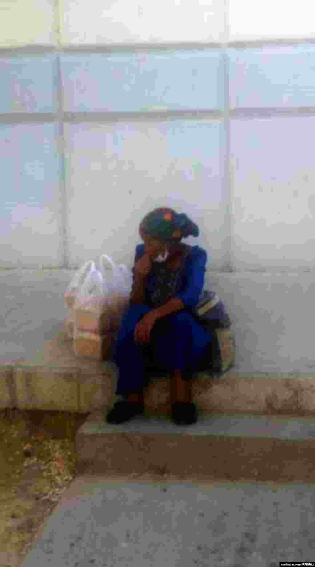 Satyn alan çöreklerine seredip oturan aýal. Aşgabat, 2021.