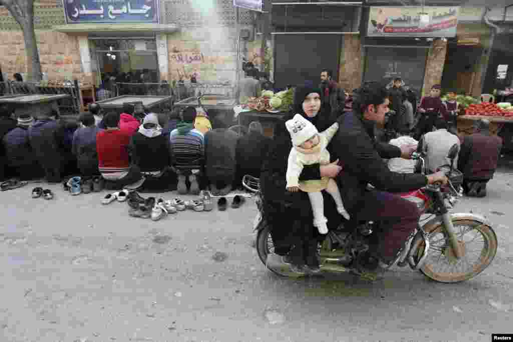 A couple with a child ride a motorcycle past demonstrators praying along a street, before a protest against Syrian President Bashar al-Assad in the Bustan al-Qasr district in Aleppo. (Reuters/Muzaffar Salman)