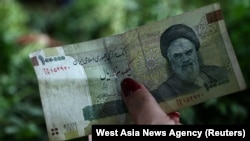 A woman holds an Iranian 100,000 rial banknote in Tajrish Bazaar in Tehran, August 1, 2019