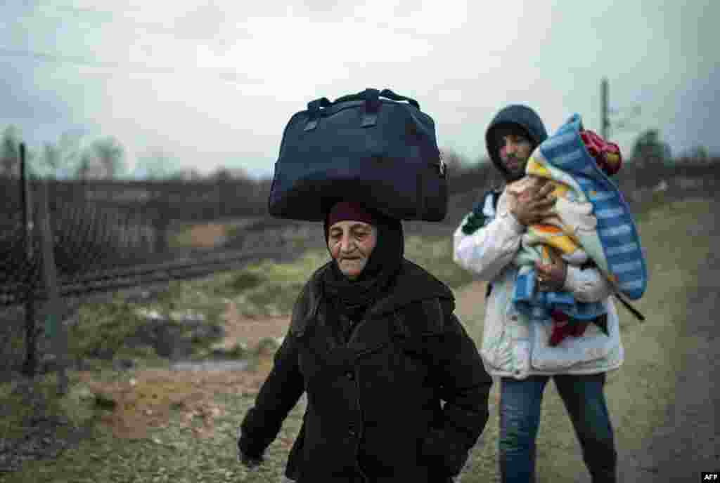 A woman balances a bag on her head and a man carries a child as migrants and refugees make their way across the Macedonia-Serbia border at Tabanovce. (AFP/Robert Atanasovski)