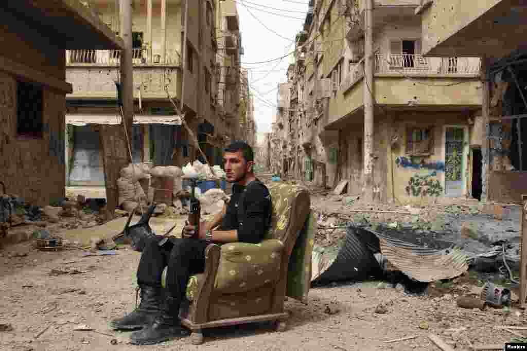A member of the Free Syrian Army holds his weapon as he sits on a sofa in the middle of a street in Deir al-Zor. (Reuters/Khalil Ashawi)