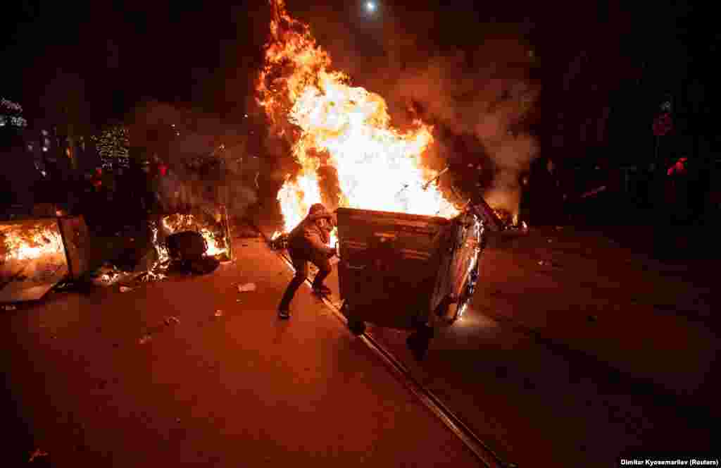 A demonstrator pushes a flaming dumpster as fights broke out between protesters and police in Sofia.