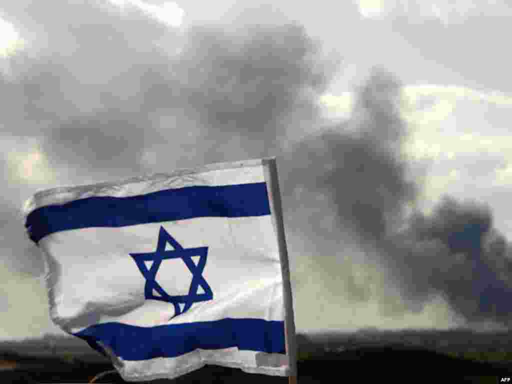 The Israeli flag flutters on a hill near the border with the Gaza Strip as smoke from Israeli strikes cover Gaza on January 9, 2009 (AFP)