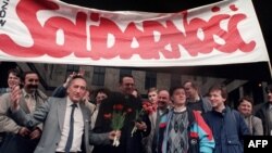 Tadeusz Mazowiecki (în costum gri, la stânga de preot) şi suporterii Solidarităţii, sărbătorind punerea mişcării în legalitate, 17 aprilie 1989
