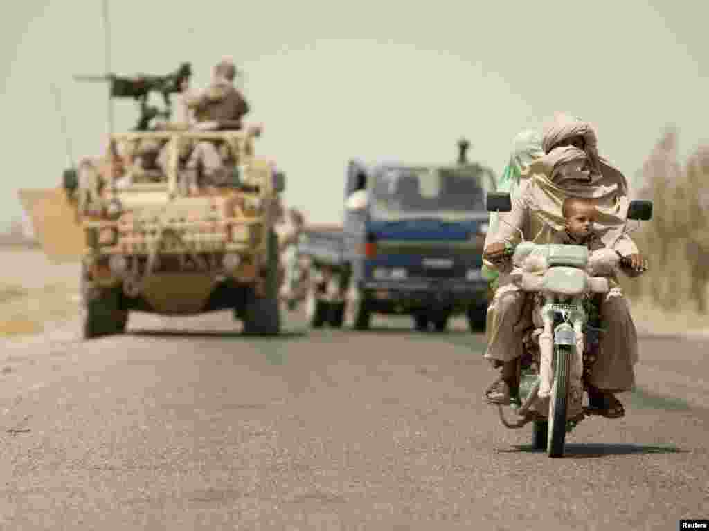 An Afghan family rides on a motorcycle in front of a British armored vehicle at a joint checkpoint with Afghan National Police outside the town of Lashkar Gah in Helmand Province.Photo by Shamil Zhumatov for Reuters