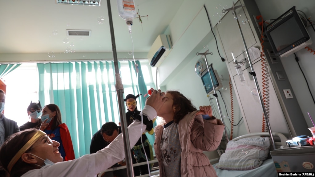 Një grua e veshur si mjeke luan me një fëmijë në spital.