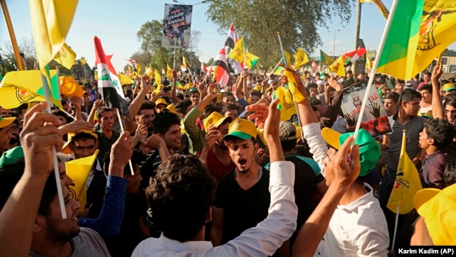 Iraqis carry paramilitary and national flags at a protest organized by the Iranian-backed Hezbollah brigades, that was active in the fight against Islamic State militants, in Baghdad, March 30, 2018