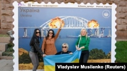 Жанчыны з украінскім нацыянальным сьцягам побач з арт-аб'ектам з выява новай маркі з Керчанскім мостам, які палае. Ілюстрацыйнае фота