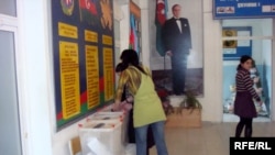 Two women push a pile of ballots into the ballot box in Baku