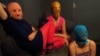 The three Pussy Riot members gathered in a darkened studio, with all three wearing the brightly colored stockings and the group's requisite balaclavas in gold, orange, and blue.