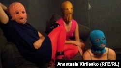 The three Pussy Riot members gathered in a darkened studio, with all three wearing the brightly colored stockings and the group's requisite balaclavas in gold, orange, and blue.