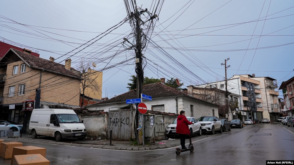 Një person kalon me trotinet pranë një shtylle e cila mëzi mban telat e rrymës dhe kabllot e telefonike dhe të internetit në lagjen "Vellusha" në kryeqytet.